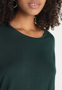 Mörkgrön, kortärmad t-shirt med rund halsringning. Mjuk, slät textur med lätt stretch. Sömmar runt halsringningen.