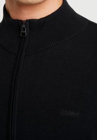 Czarny sweter na zamek z wysokim prążkowanym kołnierzem, wykonany z teksturowanej dzianiny, z subtelnym logo na piersi oraz gładkim zamkiem.
