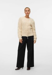 Ljusbeige stickad cardigan med kabelmönster, rund halsringning, knappframgång och knytning i midjan. I kombination med svarta vida byxor.