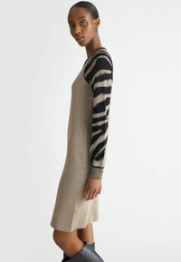 Abito a maglia con texture metallica dorata e design aderente; presenta maniche a strisce nere e dorate e polsini a coste. Indossato con stivali neri testurizzati.
