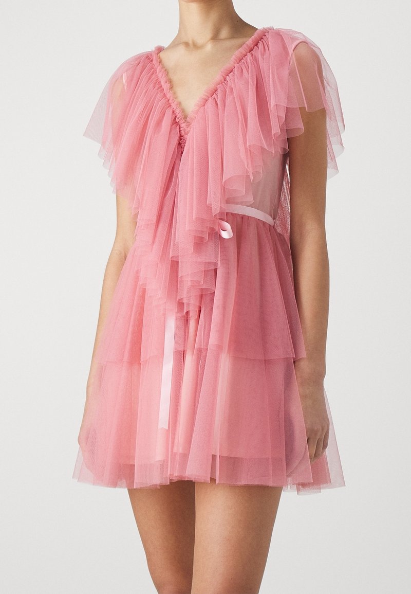 Robe en tulle rose avec des volants superposés, décolleté en V et une taille accentuée par un petit ruban en satin. Texture légère et transparente.