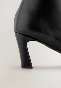 Sort hæl sko med en tekstureret læderfinish, der har et buet design og en mellem-høj blokhæl for stabilitet.