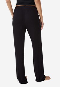 Czarne, prążkowane spodnie szerokie w nogawkach z elastycznym paskiem w talii, miękka tekstura i luźny krój, pokazane od tyłu z widocznymi gołymi stopami.