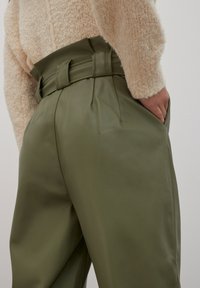 Groene faux leren broeken met een hoge taille, brede benen en riemlussen. De stof lijkt glad met subtiele plooien en zijzakken.