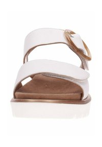 White sandal with two wide straps, a circular tan accent buckle, and a flat beige sole, featuring a suede-textured footbed.