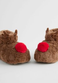 Bruna plyschtofflor med små horn och röda pom-poms på baksidan. Mjuk, lurvig textur med rundad form, utformad för komfort.
