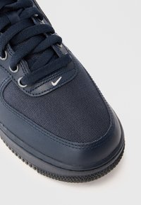 Baskets bleu marine avec une tige en toile texturée, des accents en cuir lisse, des lacets ronds et un petit logo blanc sur le côté.
