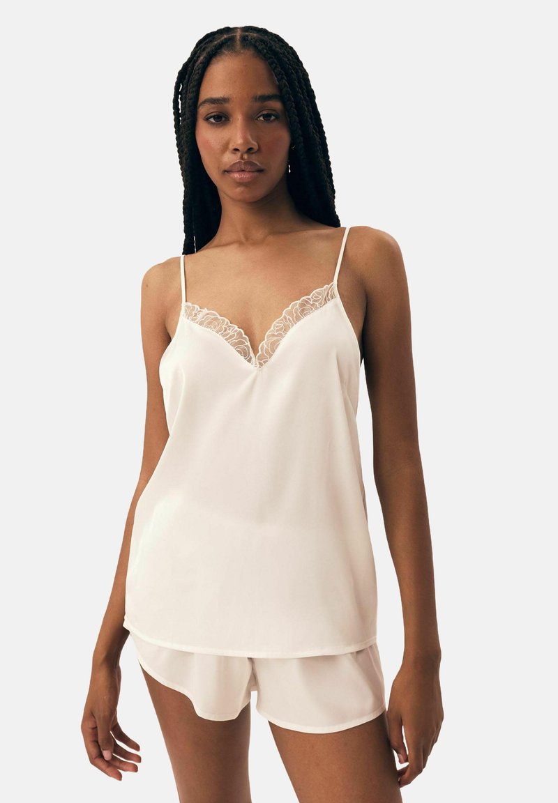 White satin camisole with lace detailing along the V-neckline, paired with white satin shorts featuring a curved hem.
