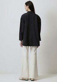 Black striped oversized shirt with a back yoke, paired with cream flared pants and beige shoes. Smooth texture, collared design.