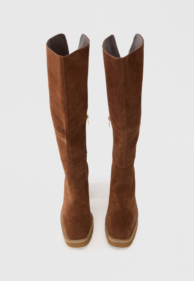 Botas de ante marrón hasta la rodilla con suela de goma plana, que presentan costuras sutiles y dos cremalleras laterales para facilitar su uso.