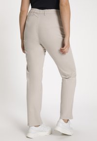 Pantaloni beige con una texture liscia, slim fit e cintura elastica. Abbinati a sneakers bianche con suola spessa.