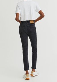 Jeans negros de talle alto y ajuste slim, con dos bolsillos traseros y una etiqueta de cuero marrón claro en la cintura. Combinados con una camiseta blanca corta.