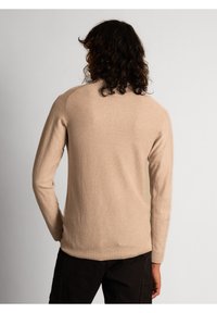 Beige pikaõlgadega kampsun, millel on soonikkoeline tekstuur. Omab ümmargust kaelust ja istuvaid varrukaid, ilma nähtavate mustrite või aktsentideta.