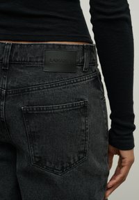 Juodos džinsinės kelnės su tekstūruotu paviršiumi, su matine juoda LAMANIA etikete juosmens srityje ir dešinėje pusėje esančiu užpakaliniu kišeniu.