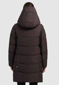 Puffjakke i mørkebrunt med kviltet design, stor hætte og cirkulært knapdetalje. Har en logoetiket på siden.