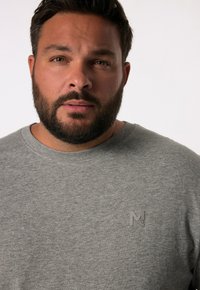 Sudadera gris con cuello redondo y puños acanalados, que presenta un pequeño logo en relieve en el pecho. Textura suave, diseño casual.