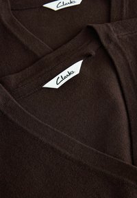 Hnedé v-neck tričká s jemnou textúrou, zobrazenie dvoch prekryvajúcich sa kusov. Nálepky označujú "Clarks" čiernym písmom na bielych štítkoch.