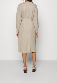 Robe tricotée beige avec ceinture, manches longues et longueur midi. Présente une texture côtelée et des fentes latérales pour faciliter les mouvements.