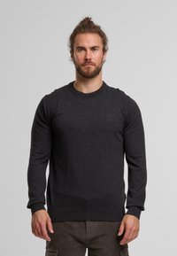 Pull à col rond gris foncé en tissu doux, avec des manches longues et un ourlet à côtes, présentant un détail de logo discret sur la poitrine.