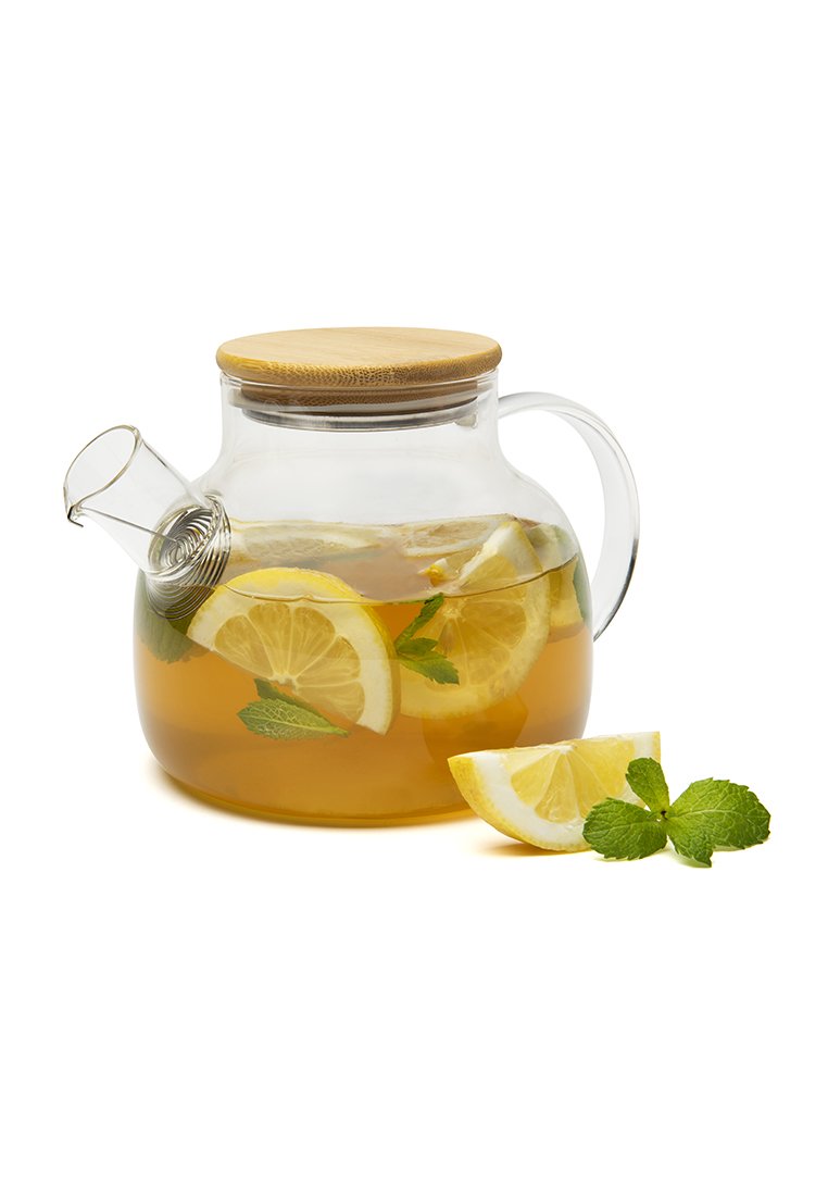 Szklany czajnik z drewnianą pokrywką, zawierający plastry cytryny i liście mięty w herbacie, w towarzystwie kawałka cytryny i gałązki mięty.