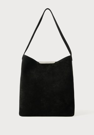 Bolsa de ombro em camurça preta com uma textura suave, design minimalista e um detalhe em metal prateado na parte superior. Apresenta uma abertura ampla.