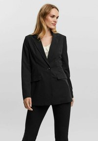 Blazer nero su misura con chiusura a un bottone, rever a forbice e due tasche frontali. Tessuto testurizzato. Vestibilità leggermente oversize.