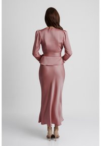 Długa satynowa sukienka w jasnoróżowym kolorze, z dopasowanym gorsetem, bufkowymi rękawami, peplum w talii oraz rozkloszowaną spódnicą, w zestawie z beżowymi butami na kostkę z paskiem.