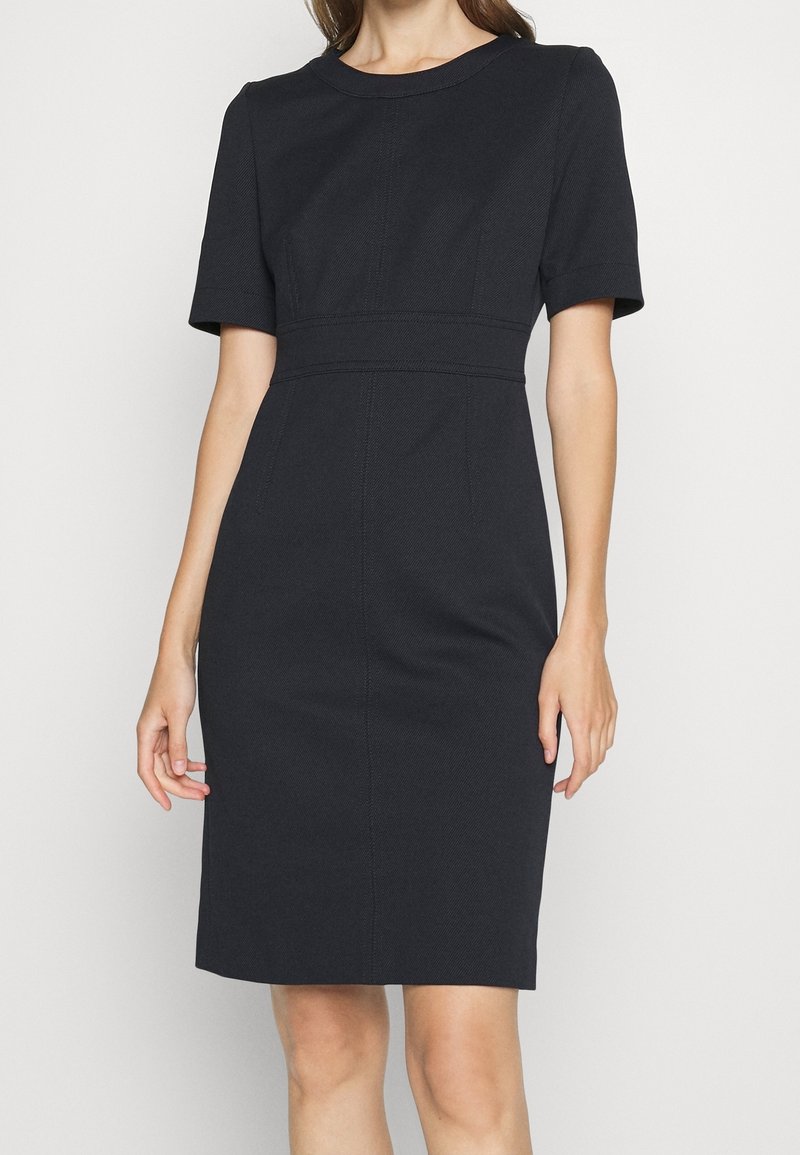 Robe ajustée noire avec manches courtes, encolure ronde et couture marquée à la taille. Tissu texturé et ourlet à hauteur des genoux.