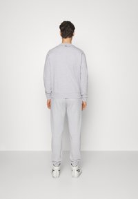 Felpa grigia in cotone e pantaloni della tuta coordinati, con polsini e vita a costine, e un piccolo logo sul retro del collo.