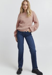 Maglione rosa lavorato a maglia con un fit rilassato e maniche a palloncino, abbinato a jeans a gamba dritta blu scuro e scarpe nere con lacci.