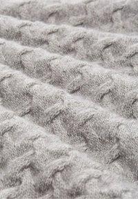 Tissu gris tricoté avec un motif torsadé texturé, présentant une finition douce et duveteuse. Le matériau semble être de la laine ou de l'acrylique.