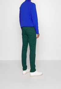 Camicia blu a maniche lunghe con colletto, abbinata a pantaloni verdi. Sneakers bianche con suole testurizzate. Design semplice, dettagli minimi.