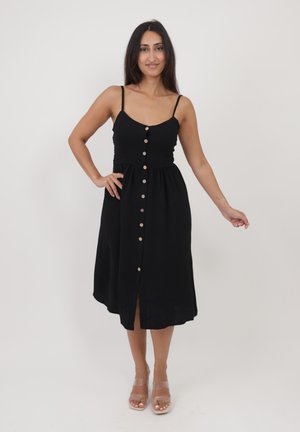 Robe noire à boutons avec bretelles spaghetti ajustables, un corsage ajusté et une jupe évasée. Elle est dotée de boutons en bois et d'une fente sur le devant.
