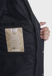 Marine parka met een gladde, geïsoleerde voering; bevat een beige label met tekst, die het dynamische ritsysteem en de weersbestendigheid beschrijft.