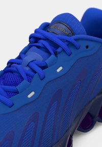 Blauwe sportieve schoen met een gestructureerde mesh bovenkant, versterkte veterogen en een gemusterde zool. Uiterst opvallende branding op de tong.