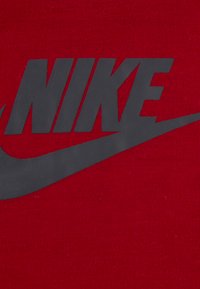 Crvena pamučna tkanina s upečatljivim crnim Nike logotipom i dizajnom swoosha. Glatka tekstura s mat završetkom tiska.