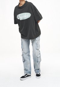 Černé oversized tričko s logem "Pegador", světle modré cargo džíny s několika kapsami a černé tenisky s bílými podrážkami.