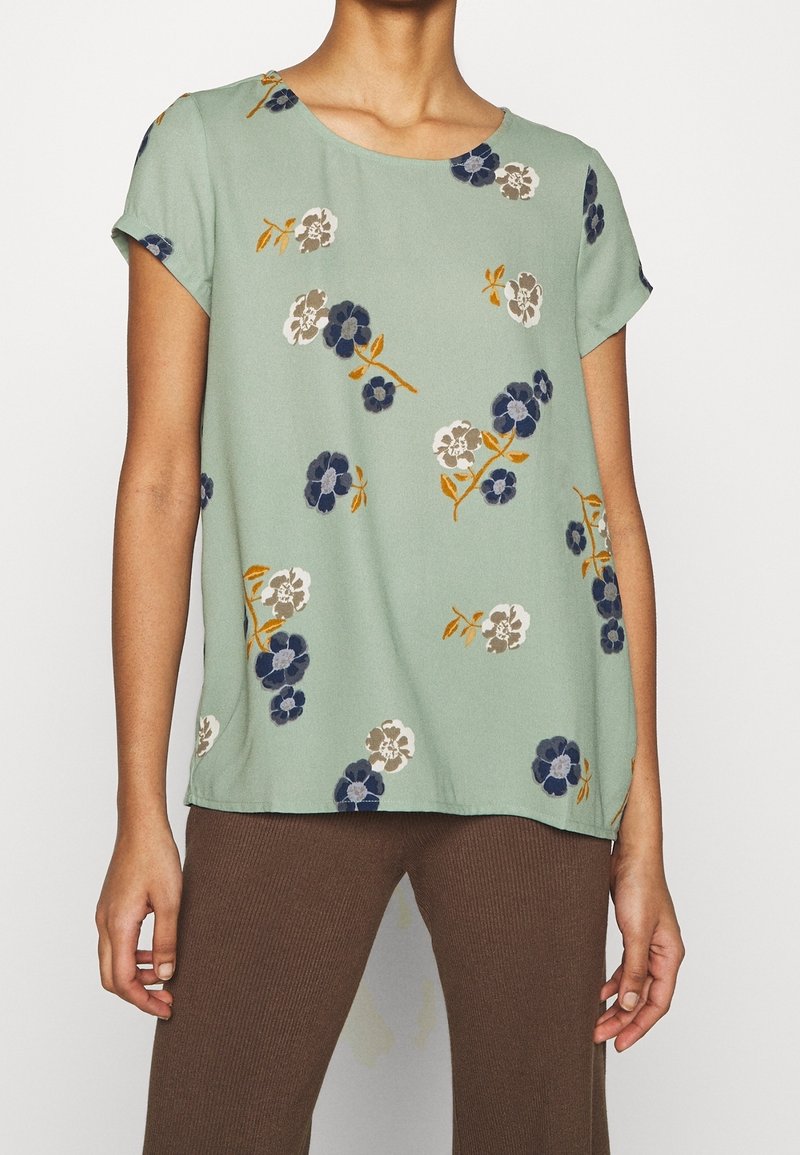 Krátký rukáv, blůza mátové barvy z lehkého materiálu se vzory květin v modré, šedé a oranžové. Kulatý výstřih a uvolněný střih.