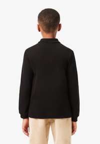 Schwarzes langärmliges Poloshirt mit Kragen, glatter Textur und gerippten Bündchen, kombiniert mit hellbeigen Cordhosen.