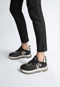 Svarta och silverfärgade sportskor med glittrande detaljer, vadderad krage och tjock vit sula, med ett mönstrat överdel.