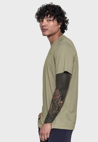 Olivengrünes Baumwoll-T-Shirt mit kurzen Ärmeln und rundem Halsausschnitt, das ein kleines Logo auf der Brust und eine lässige Passform aufweist.