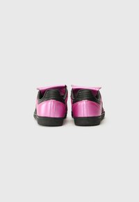 Rosa och svarta sneakers med en glänsande yta, utrustade med en vadderad krage och texturerad svart sula, sedda bakifrån.