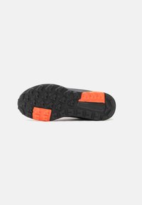 Schwarze Sportschuhsohle mit strukturiertem Muster, lebhaften orangen Akzenten und ausgeprägten Traktionsnoppen für verbesserten Halt.