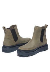 Hnědé kožené kotníkové boty s černými elastickými bočními panely a silnou černou podešví. Mají texturovaný povrch a minimální švy.