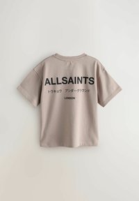 Kratkām piedurknēm beige t-krekls no kokvilnas. Aizmugurē ir melnas drukātas uzraksti, tostarp "ALLSAINTS" un "LONDON."