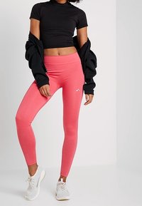 Černý přiléhavý crop top a růžové legíny s vysokým pasem a hladkou texturou. Bílé tenisky s texturovanou podrážkou.