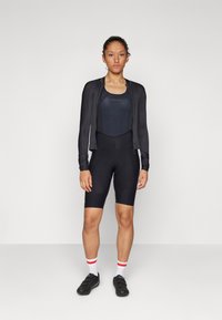 Black cycling outfit featuring a fitted short-sleeve jacket and bib-shorts. Smooth fabric with minimal seams, paired with black cycling shoes.