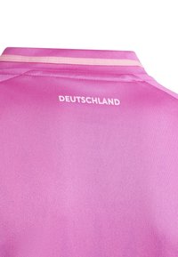 Różowa koszulka sportowa o gładkiej fakturze z kołnierzykiem. Na górnej części pleców widnieje nadruk "DEUTSCHLAND" na biało, z kontrastowymi wykończeniami.