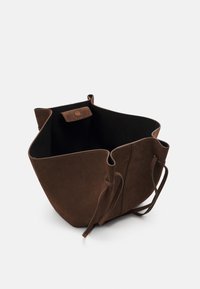 Brązowa torebka z zamszu typu tote z otwartym wierzchem, z dwiema grubymi rączkami i zapięciem na zatrzask. Wnętrze jest czarne i nie ma żadnych przegród.