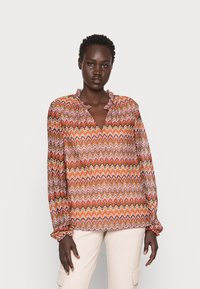 Blusa de manga longa em padrão zigzag multicolorido, com decote com babados e punhos elásticos, apresentando tons de laranja, rosa e castanho.
